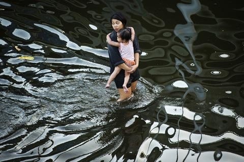 5. Một người phụ nữ bế con lội trong dòng nước lũ gần sông Chao Praya, Bangkok (Thái Lan). (Ảnh: Getty Images)